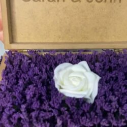 Personalized wooden flower box with "Sarah & John" engraving in Courier New font (2 cm height), filled with vibrant purple real preserved lavender and a single artificial white rose. Ideal for romantic gifts, weddings, anniversaries, or Valentine’s Day celebrations, this handcrafted keepsake box measures 21 cm L x 14 cm W x 7 cm H. The natural wood finish and aromatic lavender scent make it a timeless gift for couples to cherish forever. Crafted with love by Sear Handcrafted Elegance. Video Cover.