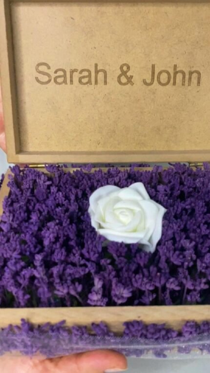 Personalized wooden flower box with "Sarah & John" engraving in Courier New font (2 cm height), filled with vibrant purple real preserved lavender and a single artificial white rose. Ideal for romantic gifts, weddings, anniversaries, or Valentine’s Day celebrations, this handcrafted keepsake box measures 21 cm L x 14 cm W x 7 cm H. The natural wood finish and aromatic lavender scent make it a timeless gift for couples to cherish forever. Crafted with love by Sear Handcrafted Elegance. Video Cover.