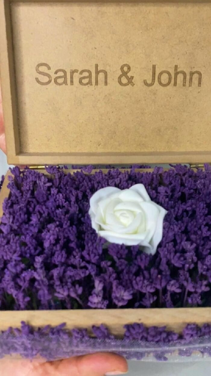 Personalized wooden flower box with "Sarah & John" engraving in Courier New font (2 cm height), filled with vibrant purple real preserved lavender and a single artificial white rose. Ideal for romantic gifts, weddings, anniversaries, or Valentine’s Day celebrations, this handcrafted keepsake box measures 21 cm L x 14 cm W x 7 cm H. The natural wood finish and aromatic lavender scent make it a timeless gift for couples to cherish forever. Crafted with love by Sear Handcrafted Elegance. Video Cover.