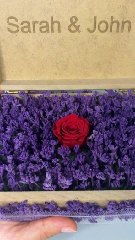 Personalized wooden flower box with "Sarah & John" engraving in Courier New font (2 cm height), filled with vibrant purple real preserved lavender and a single preserved red rose. Ideal for romantic gifts, weddings, anniversaries, birthdays, or special occasions, this handcrafted keepsake box measures 21 cm L x 14 cm W x 7 cm H. The natural wood finish and aromatic lavender make it a timeless gift for couples to cherish forever. Crafted with love by Sear Handcrafted Elegance.