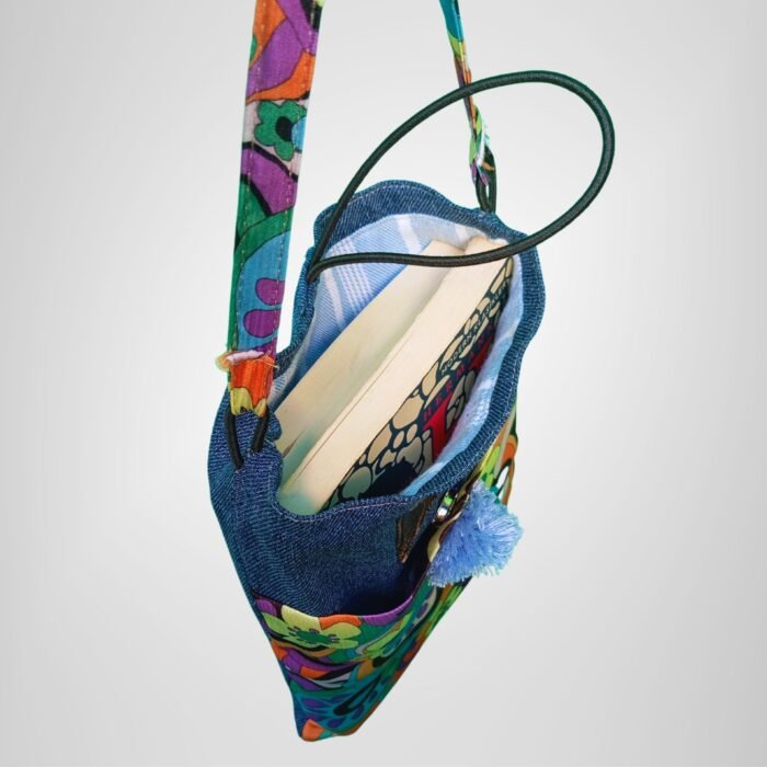 Retro psychedelic denim book bag inside view, Sear handcrafted elegance, blue pom-pom, books inside, colorful floral fabric, denim top, plaid lining.