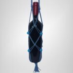 A Sear Handcrafted Elegance macrame wine bottle bag in blue, handmade from 100% recycled cotton, holding a wine bottle. The bag features an intricate knot design with blue decorative beads and a tassel at the bottom, displayed against a plain background.