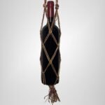A Sear Handcrafted Elegance sim macrame wine bottle bag in red, handmade with shimmering threads, holding a wine bottle. The bag features an intricate knot design with a sparkling finish and a tassel at the bottom, displayed against a plain background.