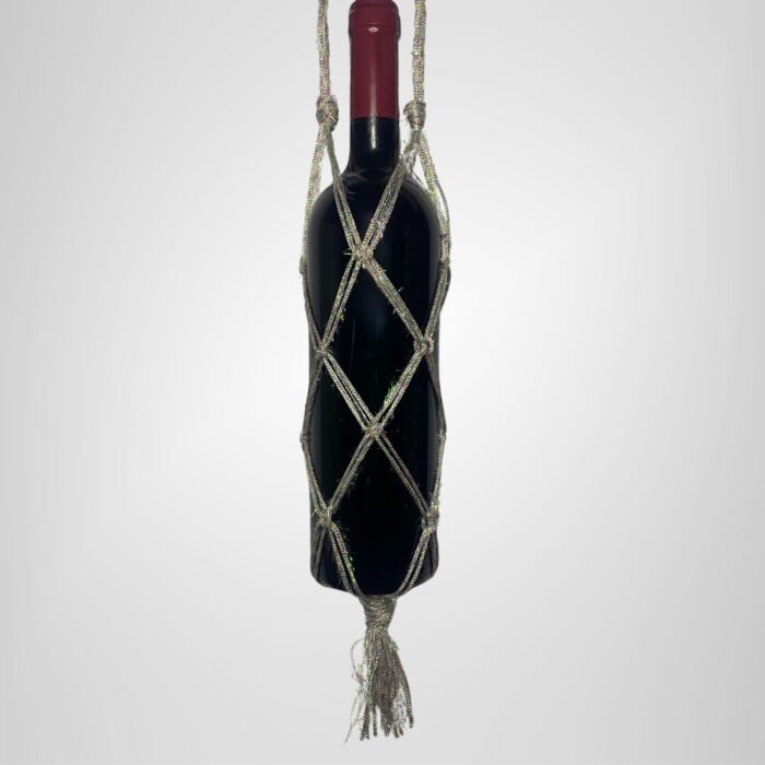 A Sear Handcrafted Elegance sim macrame wine bottle bag in silver, handmade with shimmering threads, holding a wine bottle. The bag features an intricate knot design with a sparkling finish and a tassel at the bottom, displayed against a plain background.