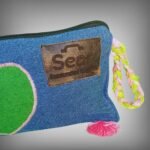 Close-up of a blue denim makeup bag by Sear Handcrafted Elegance, highlighting the green heart design with pink stitching and the pink-green braided strap detail. A trendy and functional cosmetic bag for beauty essentials.