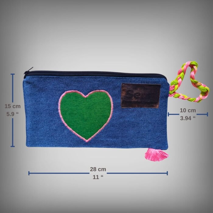 Dimensions of a blue denim makeup bag by Sear Handcrafted Elegance, measuring 28 cm (11") in length, 15 cm (5.9") in height, and 10 cm (3.94") in depth. Features a green heart design, pink stitching, a pink-green braided strap, and a pink tassel, ideal for organizing cosmetics.