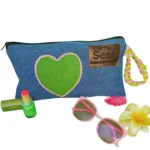 A stylish blue denim makeup bag by Sear Handcrafted Elegance, featuring a green heart design with pink stitching, a pink and green braided strap, and a pink tassel detail. This zippered cosmetic pouch is perfect for organizing beauty essentials.
