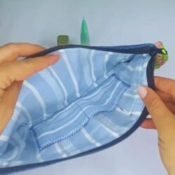 A stylish blue denim makeup bag by Sear Handcrafted Elegance, featuring a green heart design with pink stitching, a pink and green braided strap, and a pink tassel detail. This zippered cosmetic pouch is perfect for organizing beauty essentials.