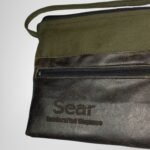 Close-up front view of a green and black leather handbag by Sear Handcrafted Elegance, showcasing the front pocket and logo. Modern and stylish design.