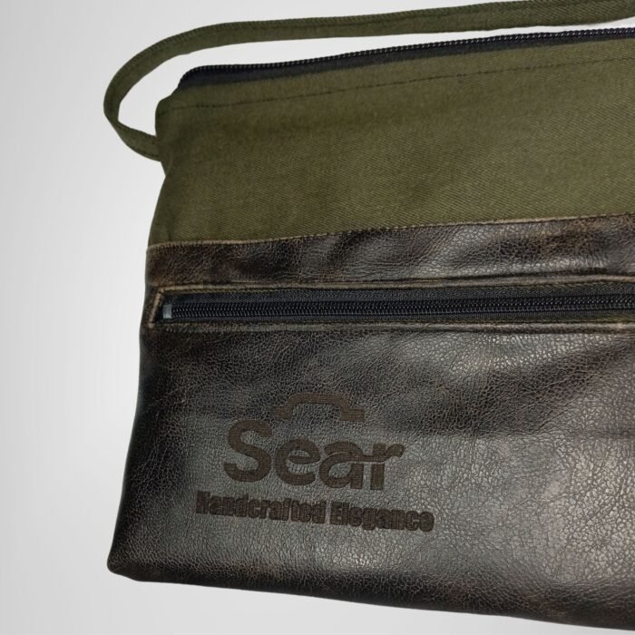 Close-up front view of a green and black leather handbag by Sear Handcrafted Elegance, showcasing the front pocket and logo. Modern and stylish design.
