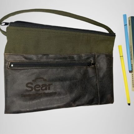 Green and black leather handbag by Sear Handcrafted Elegance, front view, placed next to a book and pens for scale. Features a front pocket and modern design.