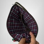 Green and black leather handbag by Sear Handcrafted Elegance, interior view held open, showing red and blue plaid lining and pens in the front pocket.