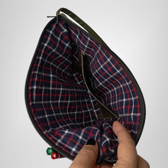 Green and black leather handbag by Sear Handcrafted Elegance, interior view held open, showing red and blue plaid lining and pens in the front pocket.