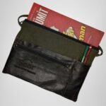 Green and black leather handbag by Sear Handcrafted Elegance, side view, holding a book and pens. Features a front pocket and modern design.
