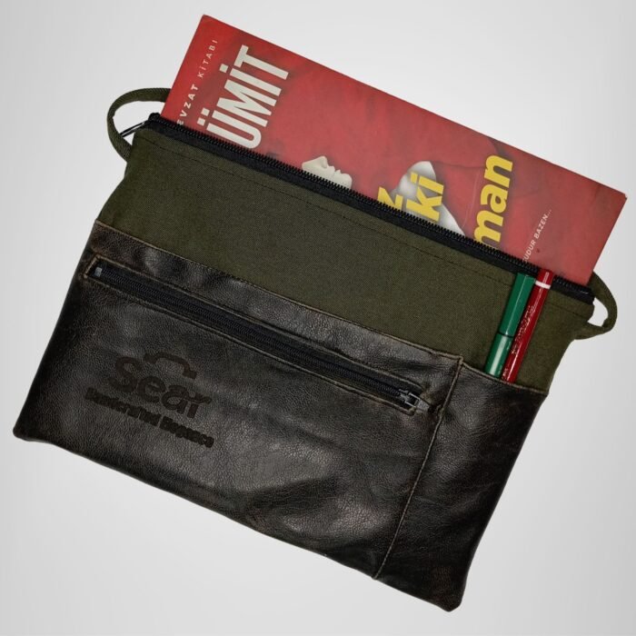 Green and black leather handbag by Sear Handcrafted Elegance, side view, holding a book and pens. Features a front pocket and modern design.