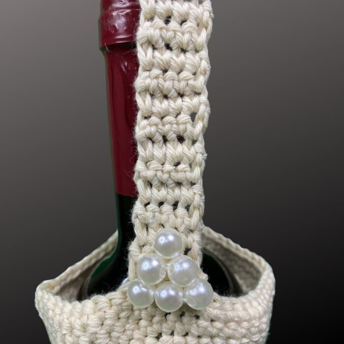Handmade beige crochet wine bottle bag holding a wine bottle, featuring elegant pearl embellishments near the strap. Crafted from certified organic cotton, this eco-friendly bag is perfect for stylishly carrying wine or water bottles.