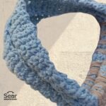 A detailed view of a handmade macrame handbag's handle by Sear Handcrafted Elegance, highlighting the blue macrame handle and beige weaving details with a leopard print linen base, against a textured white wall.