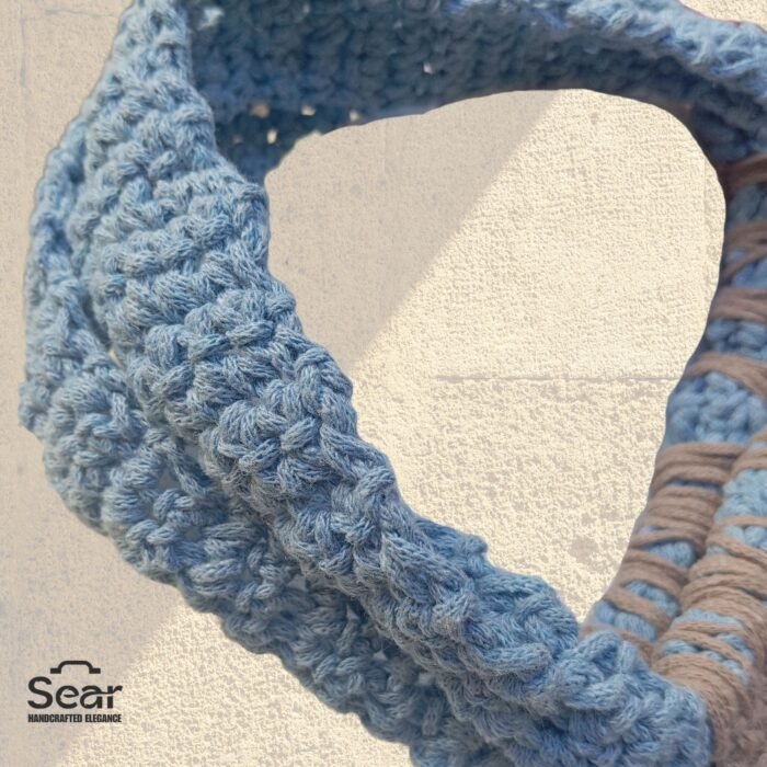 A detailed view of a handmade macrame handbag's handle by Sear Handcrafted Elegance, highlighting the blue macrame handle and beige weaving details with a leopard print linen base, against a textured white wall.