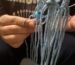 Sema, co-founder of Sear Handcrafted Elegance, crafting a macramé wine or bottle bag with light blue yarn and a turquoise bead, wearing a dark 'RAMONES' shirt